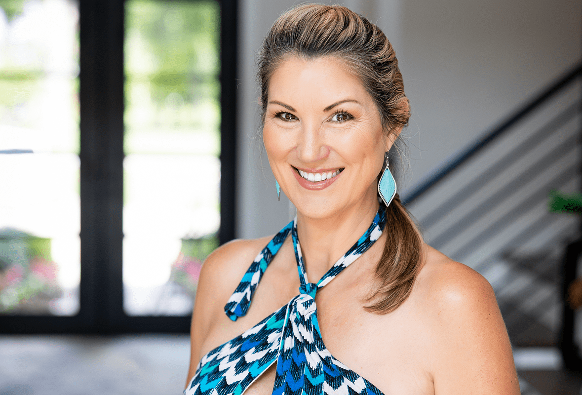 Smiling woman in blue patterned dress indoors.